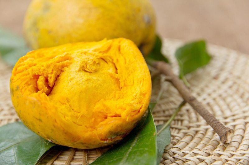 A ripe lucuma that has been partly eaten sitting on a woven mat, with a second lucuma in the background. 