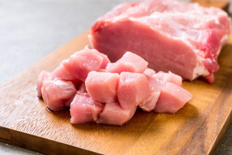 a concrete surface is a wooden chopping board with fresh chunk of meat partially cubed into pieces