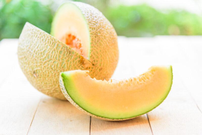 on a wooden surface is a fresh melon partially opened, the sliced melon lying beside it