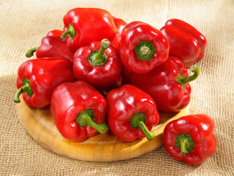 fresh red bell peppers on a round wood plate