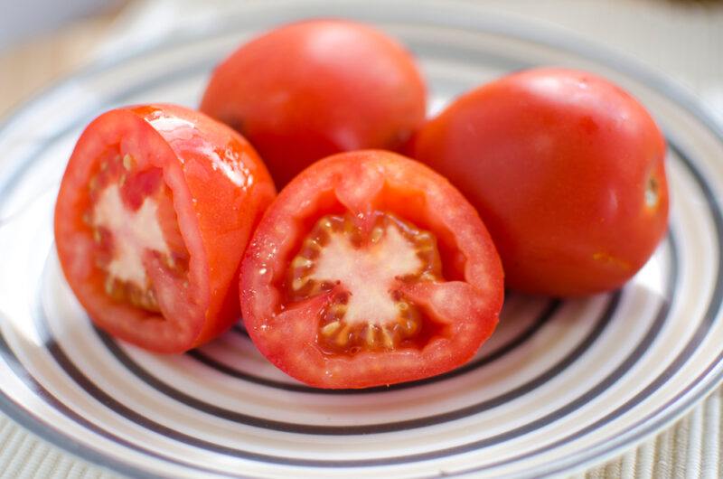 a closeup image of a whole and cut tomatoes on a white dish with circular designs