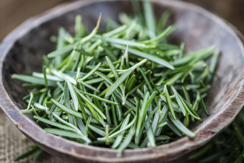 closeup image of a wooden bowl with chopped fresh rosemary