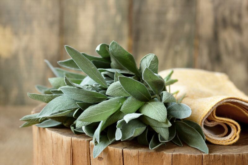 on a wooden chopping board is a bunch of fresh sage with a brown table napkin