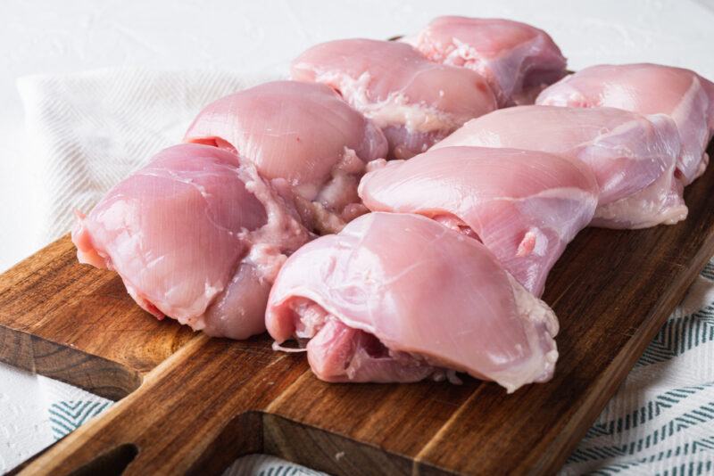 on a striped white and powdered blue table napkin is a wooden chopping board lined with 8 pieces of skinless chicken meat