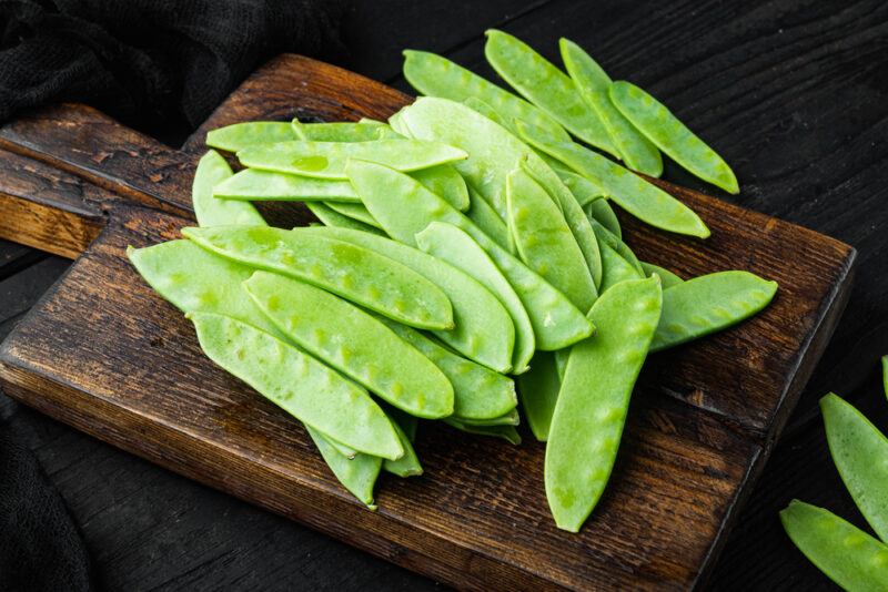 on a dark wooden chopping board are fresh trimmed snap peas