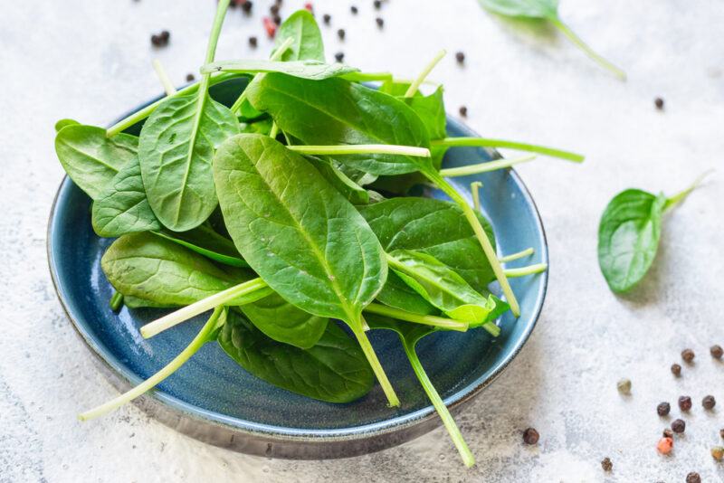 on a marble surface is a blue plate with fresh spinach with loose spinach, and black, white, and pink peppercorns