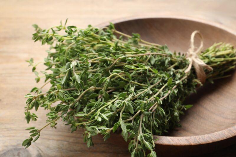 on a wooden surface is a wooden bowl with a bunch of fresh thyme