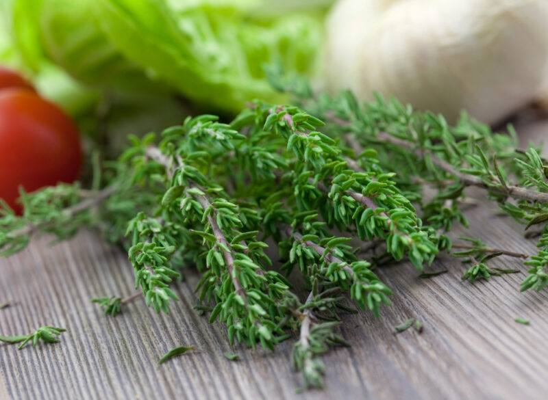 on a wooden surface is a closeup image of a bunch of fresh thyme with other veggies at the back