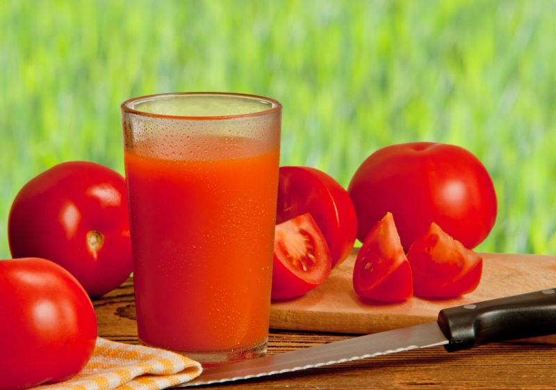 a glass of fresh tomato juice surrounded by whole and sliced tomatoes