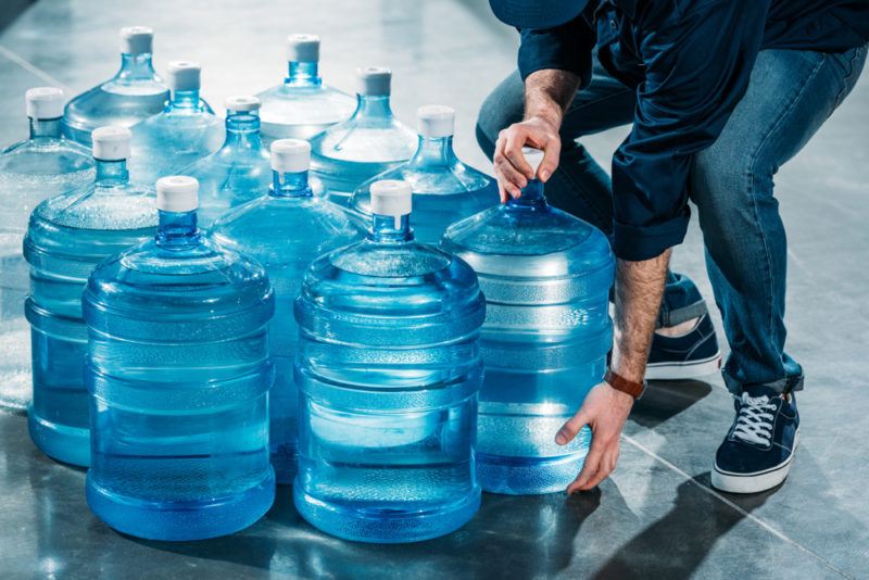 jugs of water sitting in rows with a man picking up one jug to deliver it