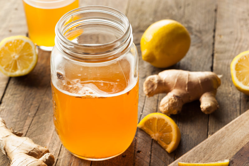 fresh kombucha placed in a mason glass jar, with fresh ginger and lemon at the background