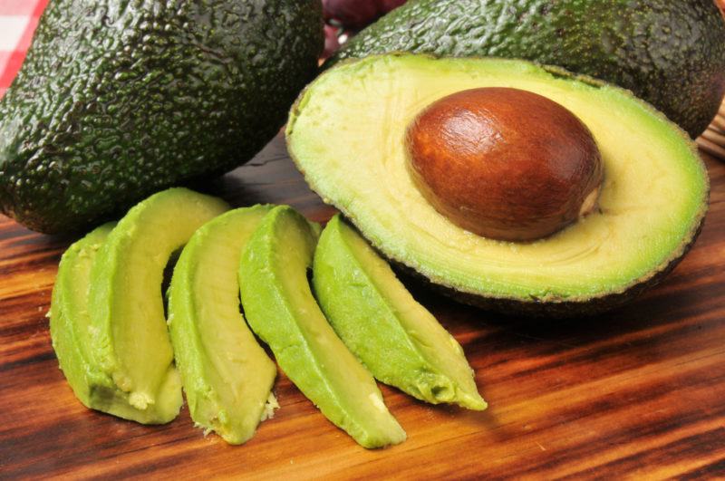 whole fresh and sliced avocado on top of a wooden table.