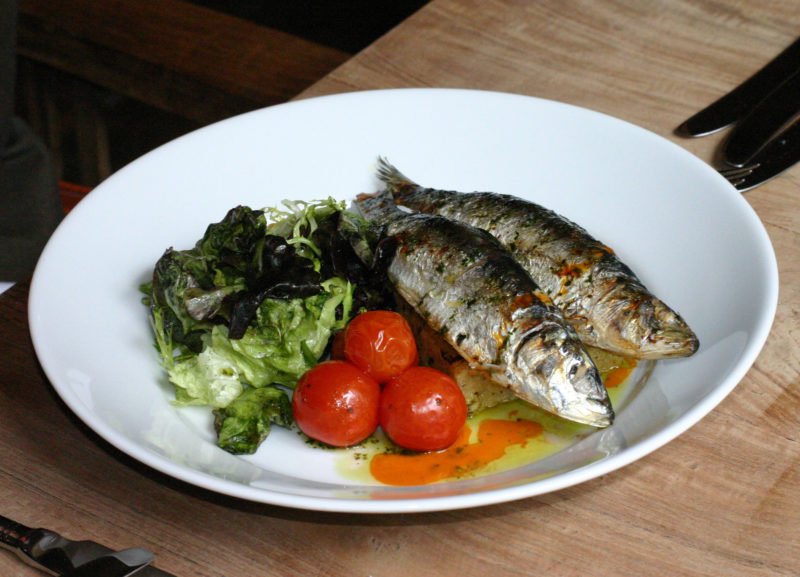 fried sardines served with romatoes and leafy greens | Food For Net two fried sardines on a white plate, served with three cherry tomatoes and lettuce