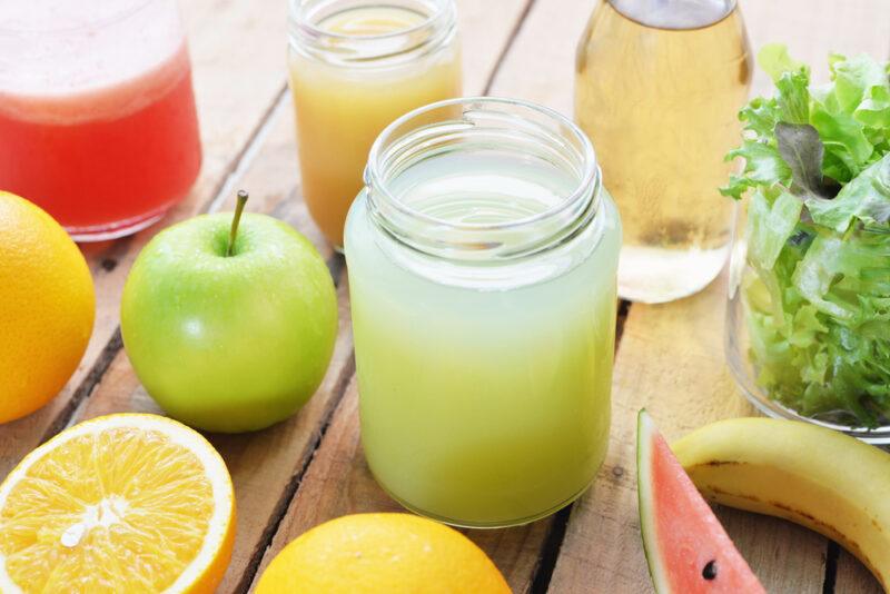 a rustic looking wooden surface with mason jars with different fruit juices with different fresh fruits around it