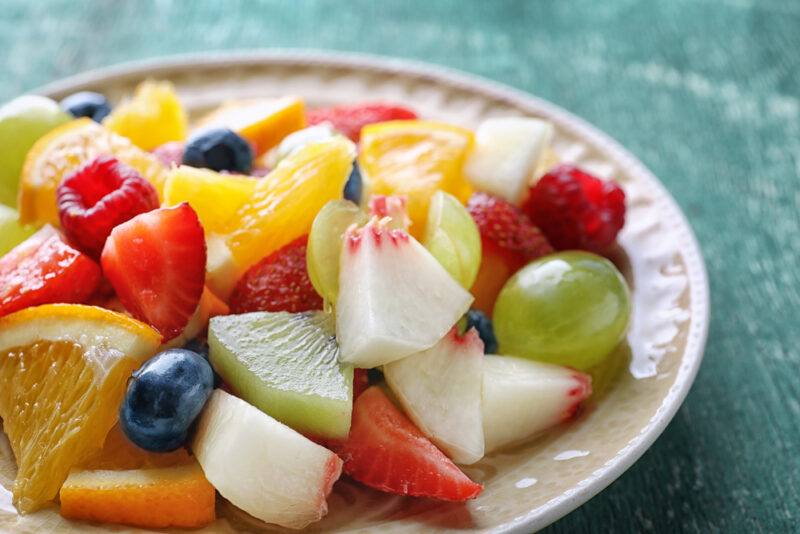 on a green-colored surface is a closeup image of a white dish full of different kinds of fruits that are cut into bite size pieces