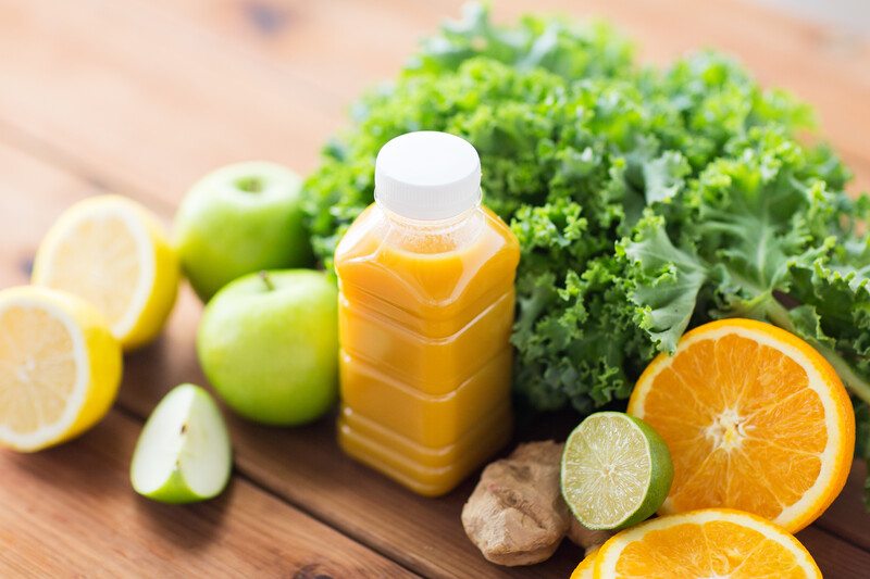 on a wooden surface are fruits and vegetables around a bottle of orange juice