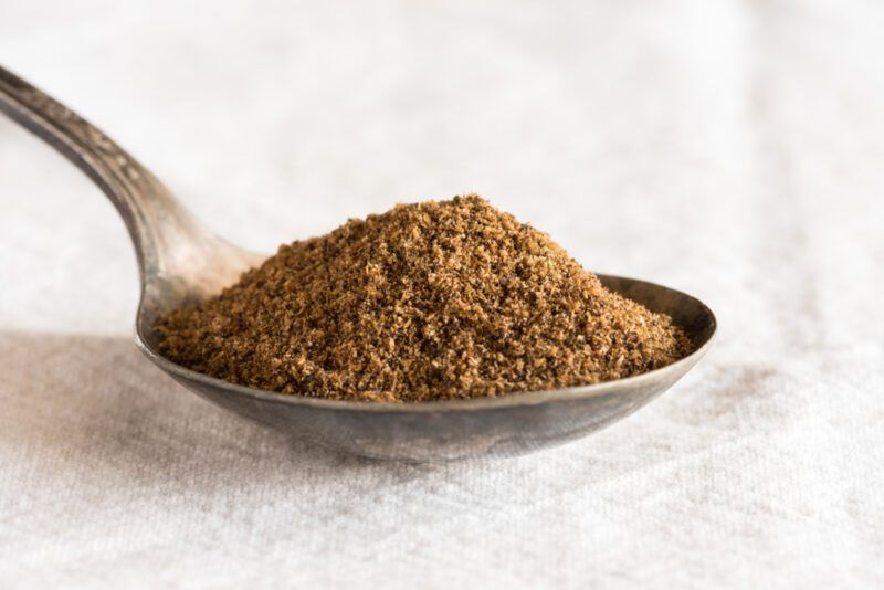 a closeup image of a silver spoon with garam masala resting on top of a white table napkin