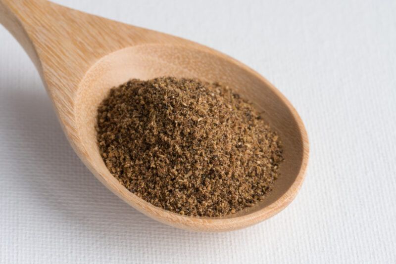 on a white surface is a wooden ladle with garam masala spice