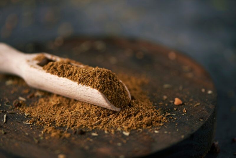 a wooden scoop with garam masala on a big round aged wooden chopping board