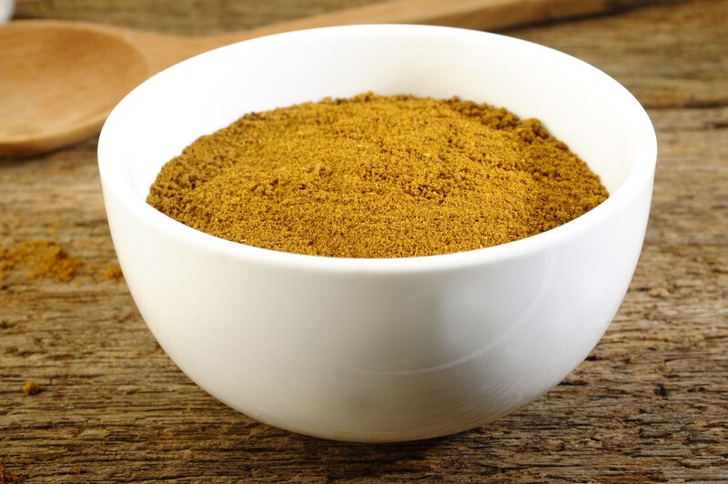 on a wooden surface is a closeup image of a white ceramic bowl full of garam masala