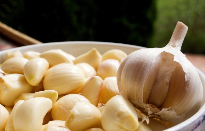 closeup image of a white bowl with peeled garlic cloves with one garlic head on top