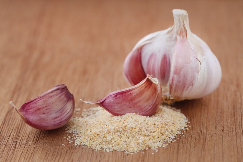 garlic head with a couple of garlic cloves on garlic powder, resting on a wooden surface