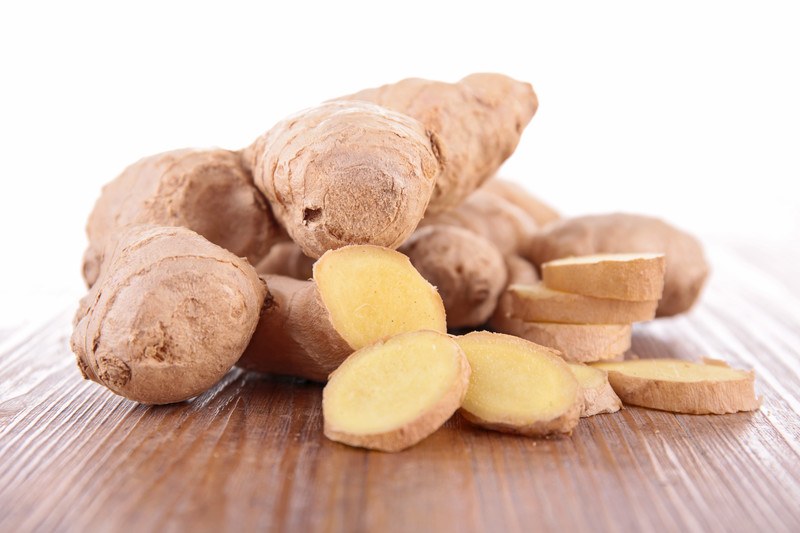 closeup image of ginger with a few sliced ones resting on a wooden surface