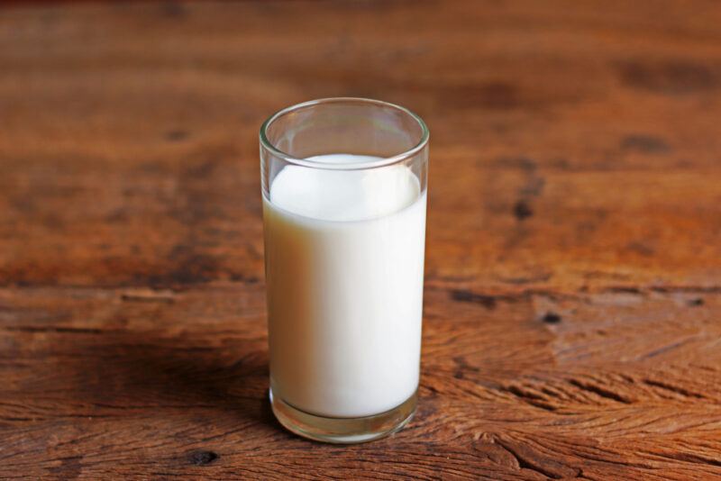 on a dark brown rustic-looking wooden surface is a glass of milk