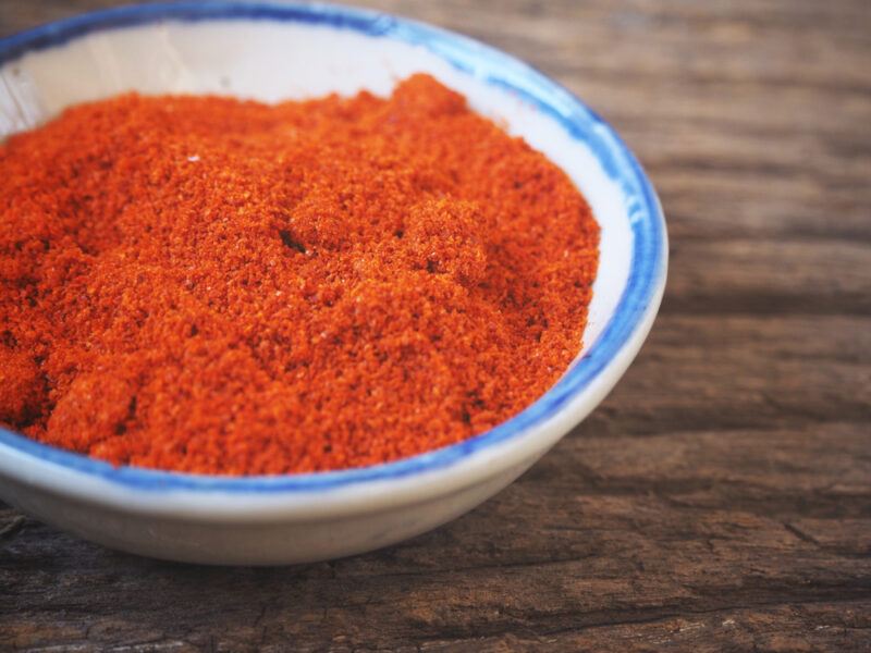 on a wooden surface is a white bowl with blue rim full of gochugaru