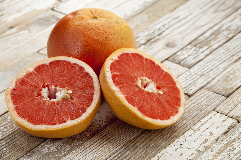 closeup image of a wooden surface with one whole grapefruit and one cut in half