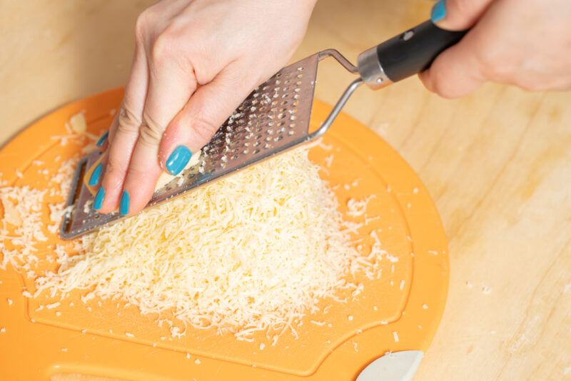 a couple of hands grating cheese on a round yellow chopping board, resting on a wooden surface