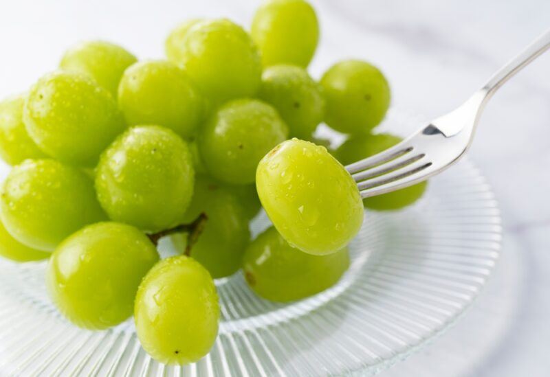 on a white surface is a clear glass plate with a bunch of green grapes with a silver fork