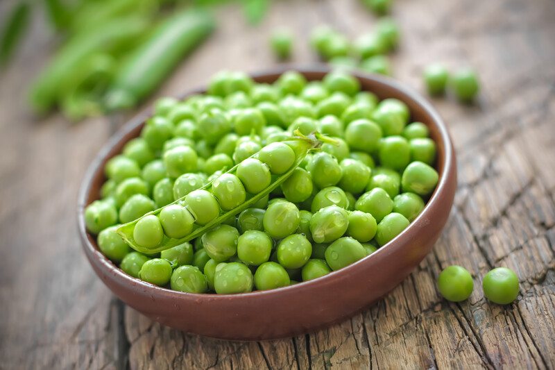 A bowl of fresh shelled green peas rests on a rustic wooden tabletop.