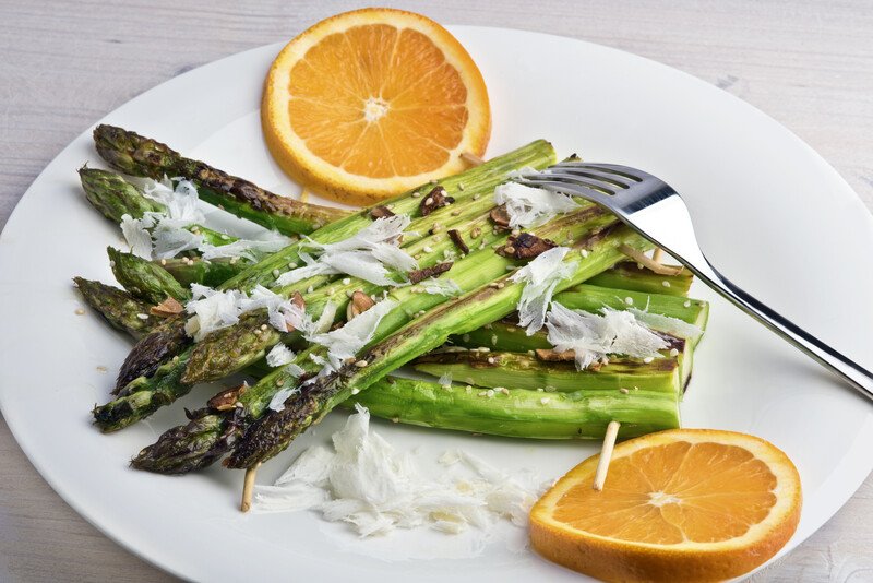 beautifully plated grilled asparagus with shaved parmesan and a couple of orange slices, with a silver fork on it