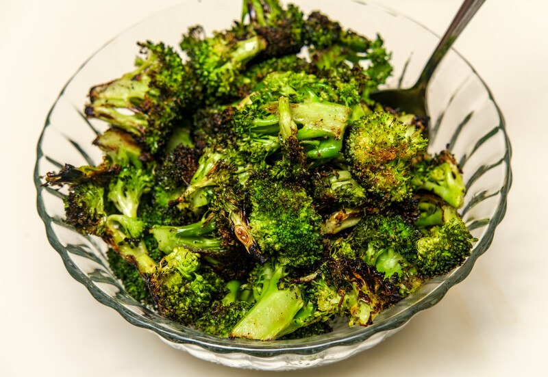 a closeup image of a clear glass bowl full of grilled broccoli