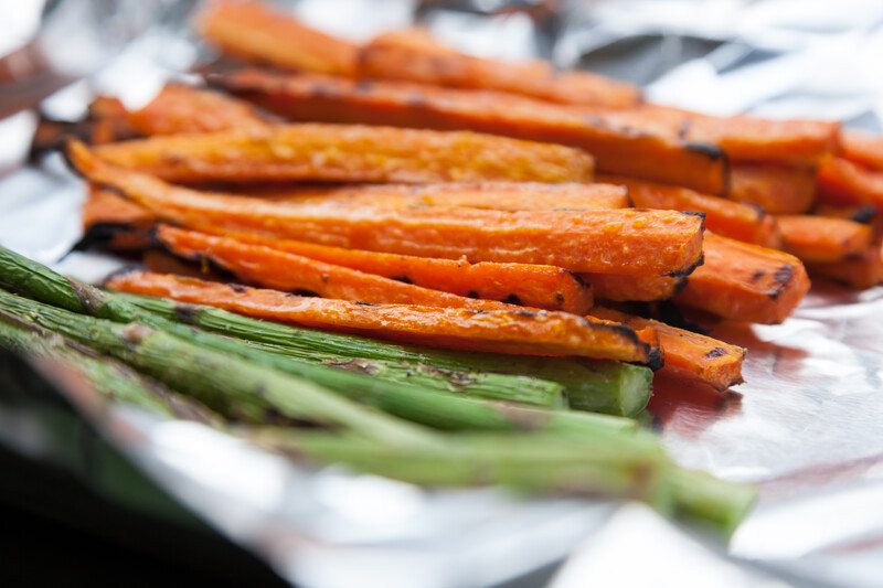 closeup image of a foil with grilled carrots and asparagus, with focus fixed on the grilled carrot sticks