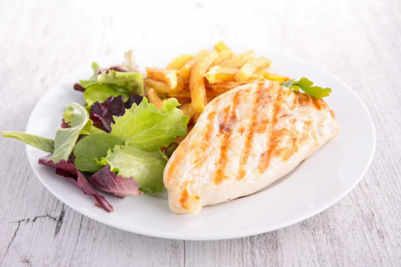 grilled skinless chicken breast served with salad and French fries.