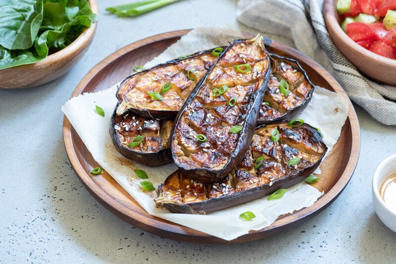 a beautifully plated grilled eggplant on a wooden plate, sprinkled with chopped fresh herbs