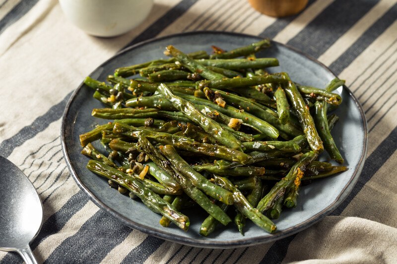 grilled green beans on a bluish ceramic dish, resting on a white and blue table cloth