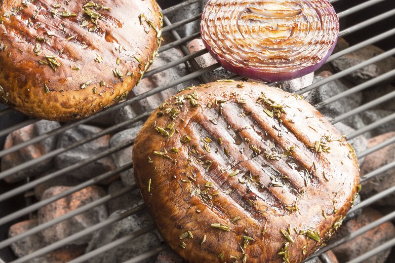 on a grill is a couple of Portobello mushrooms and a sliced red onion with visible grill marks and chopped herbs on top