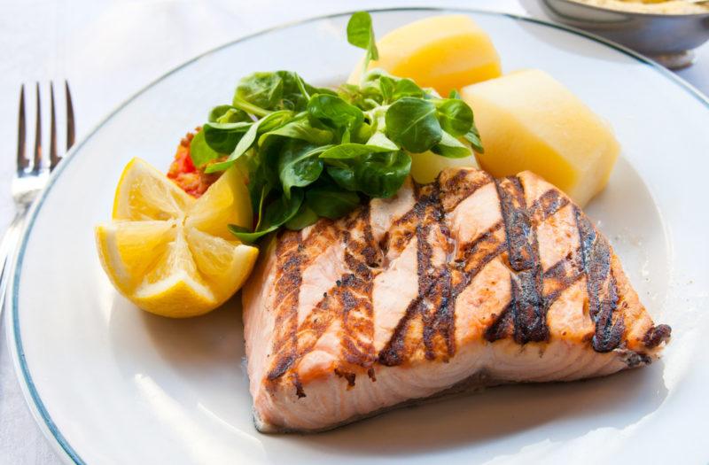 grilled salmon steak, served with lemon wedge, potatoes and green salad on a white plate.