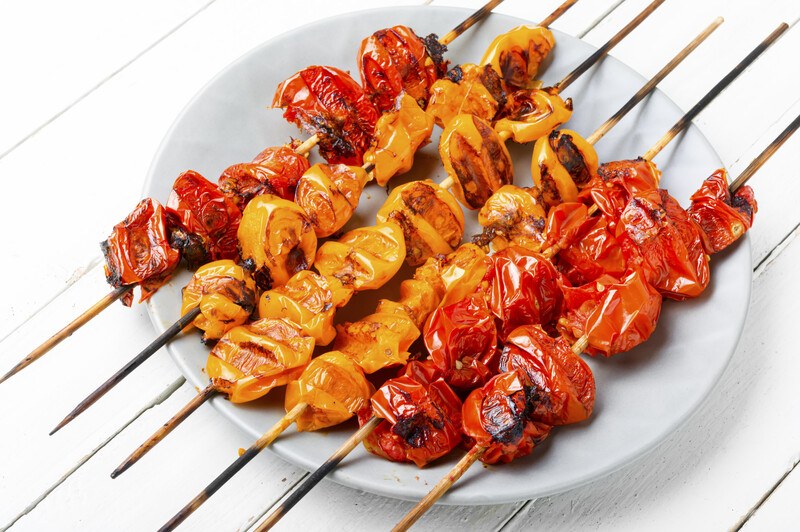 closeup image of grilled red and yellow tomatoes in skewers on a white dish