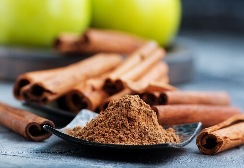 a black square dish full of ground cinnamon, with cinnamon sticks at the back