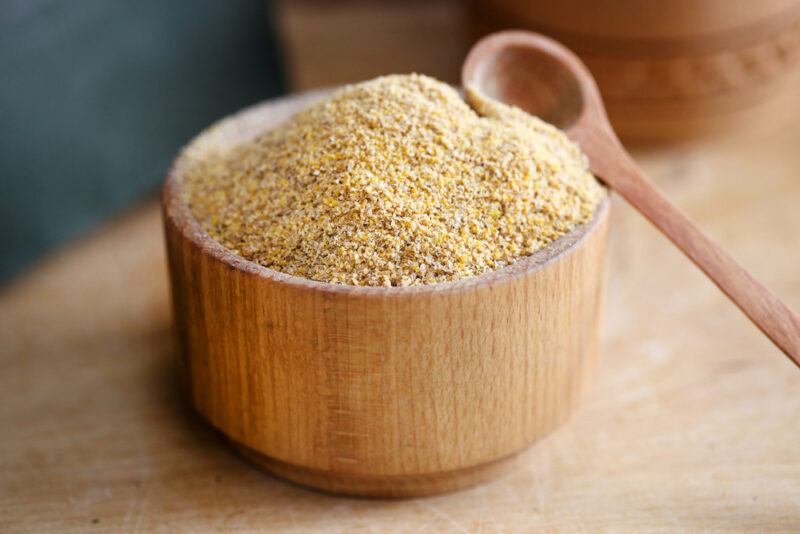 on a wooden surface is a wooden bowl full of ground mustard with a wooden spoon