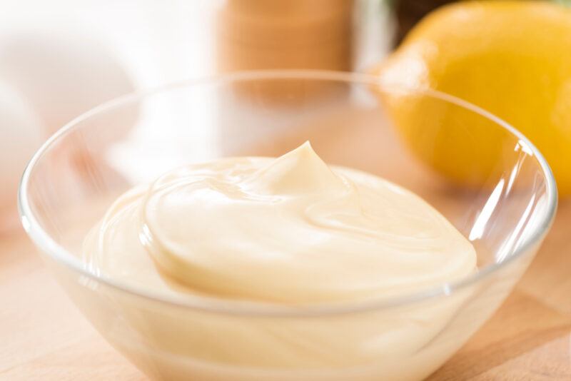 clear glass bowl with homemade mayonnaise with a whole lemon, eggs, and pepper shaker at the back