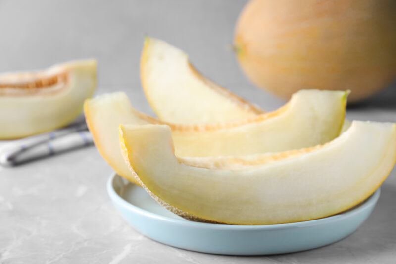 a closeup image of sliced honeydew melon on a white dish with whole honeydew melon at the back