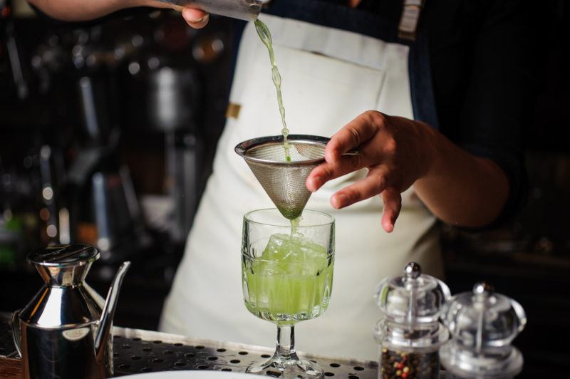 hop infused gin cocktail with bartender filtering drink and pouring into glass