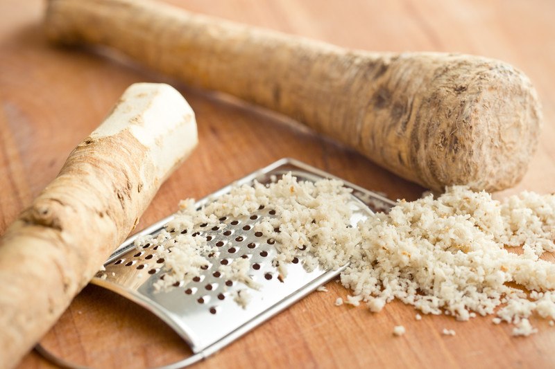 a closeup image of a couple of horseradish and a metal grater with grated horseradish on it and its side