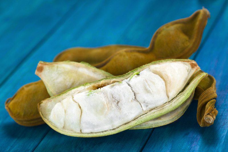 Ice cream beans on a blue table. Some have their pods opened while others are in closed pods instead. 