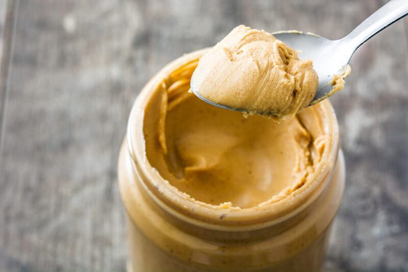 a closeup image of an open jar of peanut butter with a silver spoon also with peanut butter